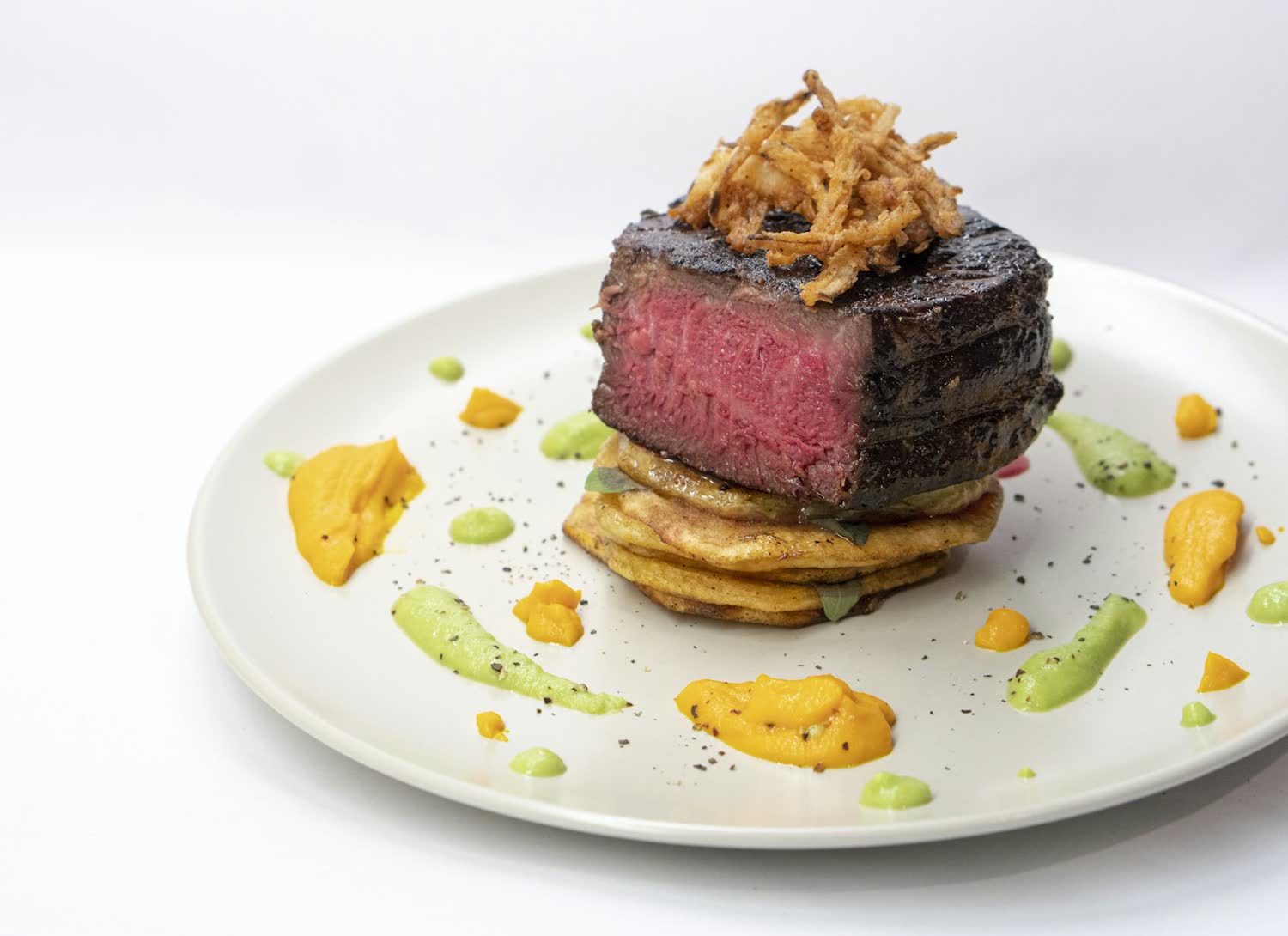 Aged beef sirloin plated with charred onion and herb oil